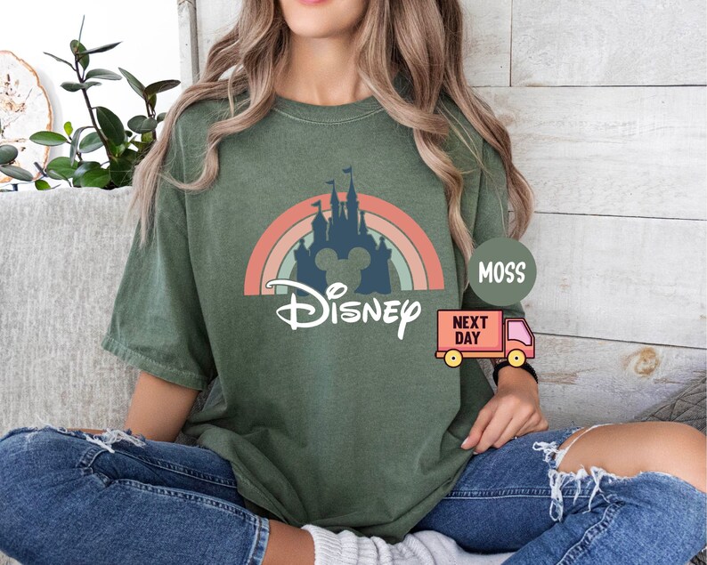 May include: A green t-shirt with a retro rainbow and a silhouette of Cinderella's castle with Mickey Mouse ears. The text "DISNEY" is printed below the castle.