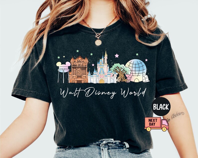 May include: Black t-shirt featuring a colorful graphic of Walt Disney World landmarks, including Cinderella Castle and Spaceship Earth. The words "Walt Disney World" are written in a script font below the graphic. The shirt is a dark color.