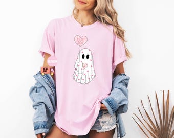May include: A pink t-shirt with a white ghost holding a pink heart balloon that says "Be My Boo". The ghost is covered in small pink hearts.