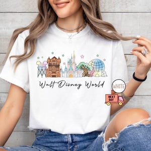 May include: White t-shirt featuring a colorful illustration of Walt Disney World landmarks, including Cinderella's castle and Spaceship Earth. The words "Walt Disney World" are written in a script font below the graphic.