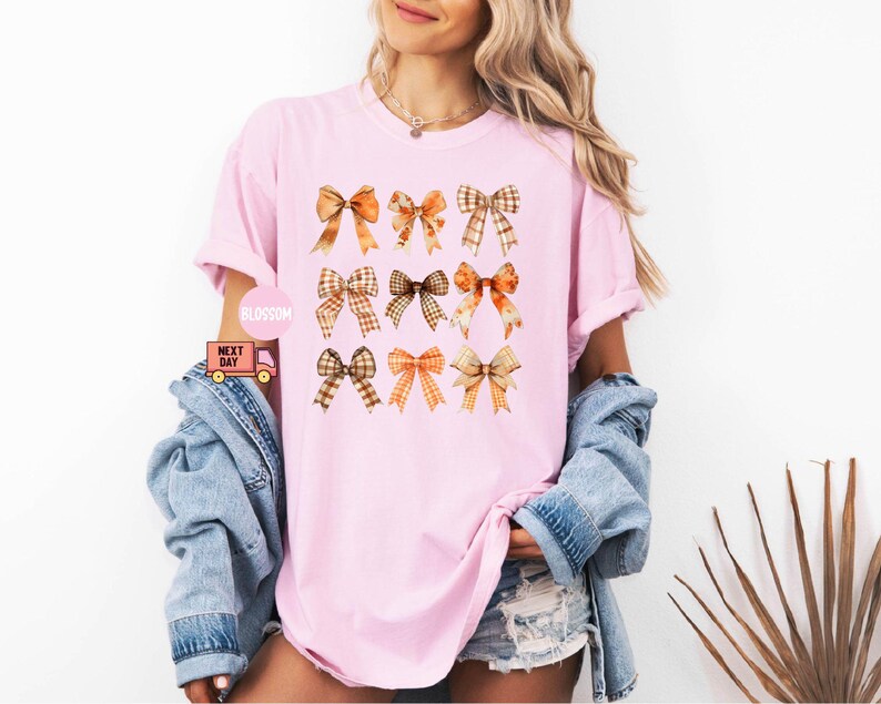 May include: A pink t-shirt with a pattern of nine orange and brown bows. The bows are arranged in three rows of three.