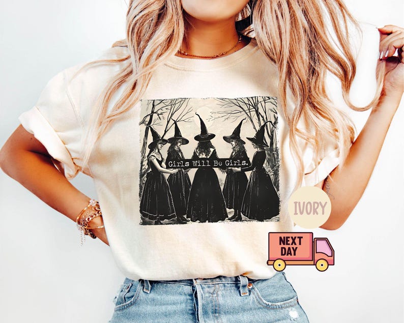 May include: A white t-shirt with a black and white illustration of four witches wearing black dresses and pointy hats. The text "Girls Will Be Girls." is printed on the shirt.
