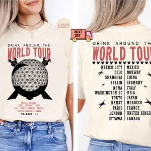 May include: Cream-colored t-shirt with the text "DRINK AROUND THE WORLD TOUR" in red. The front features a black and white geometric globe design with the text "MEXICO NORWAY CHINA GERMANY ITALY USA JAPAN MOROCCO FRANCE UNITED KINGDOM CANADA ORLANDO FL".