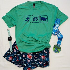 May include: A green t-shirt with a running figure, the number 50, and a silhouette of the United States. The shirt is paired with blue and white floral shorts and a blue and white running medal.
