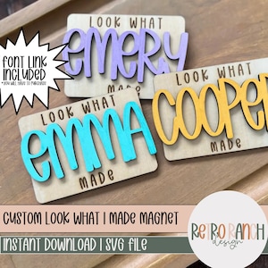 以下が含まれることがあります： 「Look What I Made」というテキストと、「Emma」、「Cooper」、「Emery」という名前がカラフルな手書き文字で書かれた木製のマグネット3つ。マグネットは木製の表面の上に置かれている。