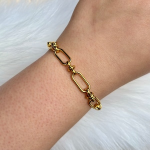 May include: A gold chain bracelet with oval links. The bracelet is on a person's wrist.