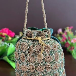 Puede incluir: Un bolso de cordón de terciopelo verde con un diseño de cuentas doradas. El bolso tiene una correa de cadena dorada.