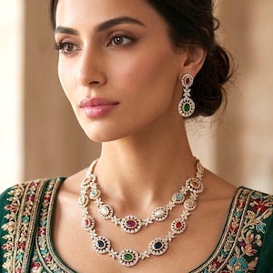 Puede incluir: Una mujer con un collar de dos hilos y pendientes a juego. La joyería presenta una serie de piedras preciosas de colores engastadas en un metal dorado. La mujer lleva un top verde bordado.