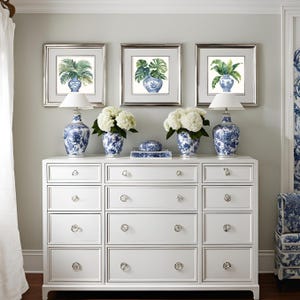 Puede incluir: Una c&oacute;moda blanca con 12 cajones y pomos de cristal. Tres impresiones enmarcadas de plantas verdes en jarrones de porcelana azul y blanco se muestran sobre la c&oacute;moda. Dos l&aacute;mparas blancas con bases de porcelana azul y blanco est&aacute;n a cada lado de las impresiones. Hortensias blancas est&aacute;n en jarrones de porcelana azul y blanco sobre la c&oacute;moda.