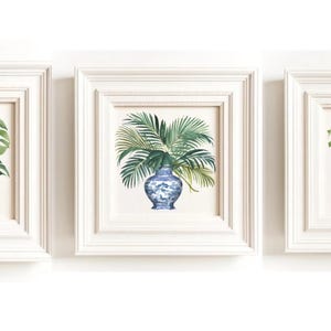 Puede incluir: Tres impresiones enmarcadas blancas con jarrones de porcelana azul y blanco llenos de hojas tropicales verdes. Las impresiones est&aacute;n dispuestas en una fila.