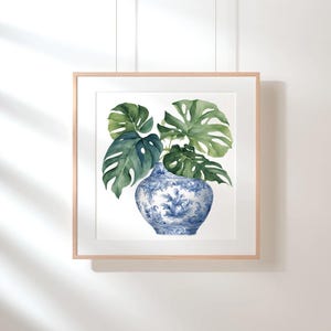 Puede incluir: Una pintura de acuarela enmarcada de un jarr&oacute;n de porcelana azul y blanco con hojas verdes de monstera.