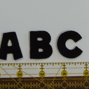 May include: Black felt letters spelling out "ABC" on a white surface with a ruler underneath.