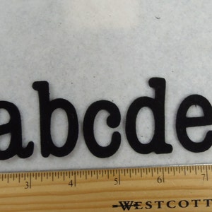 May include: Black felt letters spelling out the word "abcde" on a white surface. The letters are about 1 inch tall and are arranged in a straight line.