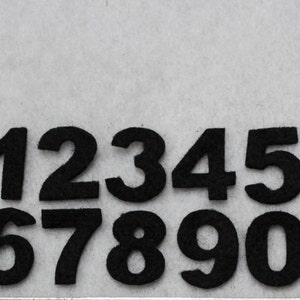 May include: Black felt numbers 1 through 0 on a white background.