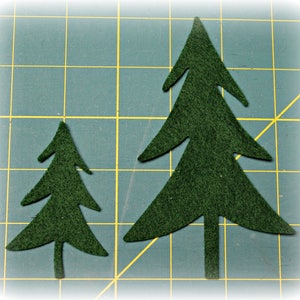 May include: Two dark green felt Christmas tree cutouts of different sizes are displayed on a green cutting mat with a grid pattern. The trees have a simple, stylized design, perfect for crafting or holiday decorations.