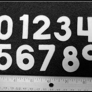 May include: White felt numbers 0 through 9 on a black background. The numbers are approximately 2 inches tall.