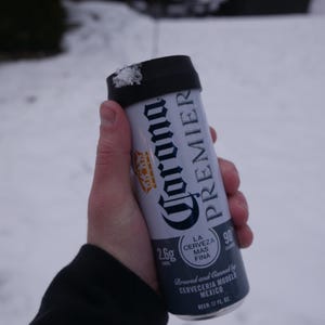 May include: A silver can of Corona Premier beer with a black pull tab. The can is 12 fluid ounces and has a 2.6g calorie count. The text on the can reads "La Cerveza Mas Fina" and "Brewed and Canned by Cerveceria Modelo Mexico".