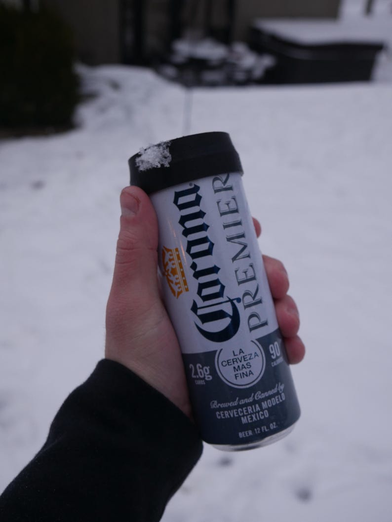 May include: A silver can of Corona Premier beer with a black pull tab. The can is 12 fluid ounces and has a 2.6g calorie count. The text on the can reads "La Cerveza Mas Fina" and "Brewed and Canned by Cerveceria Modelo Mexico".