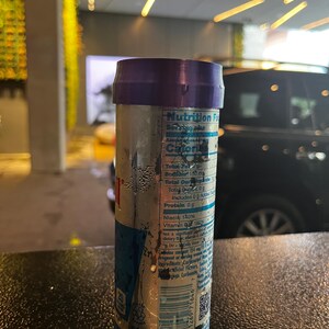 May include: A silver can of energy drink with a purple top and a nutrition facts label. The can is wet and has condensation on it. The can is sitting on a black surface.