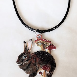 May include: A black cord necklace with a brown rabbit charm. The rabbit is surrounded by red and white mushrooms.