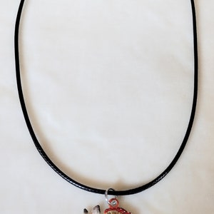 May include: A black cord necklace with a pendant featuring a brown rabbit with red and white mushrooms.