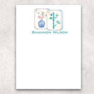 May include: A white stationery sheet featuring two rectangular tiles at the top. The left tile shows a blue and white vase with pink flowers and the number 2. The right tile displays a green bamboo stalk and the number 4. The text SHANNON WILSON is printed below.