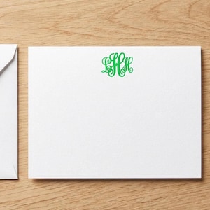 May include: A white rectangular stationery card featuring a centered green monogram with the letters L, H, and H in a decorative script font. The card is accompanied by a matching white envelope positioned to the left of the main card.