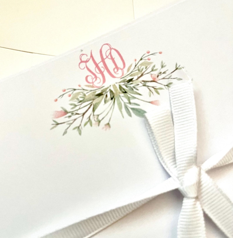 May include: A white envelope with a pink floral design and the monogram "HO" in pink. The envelope is tied with a white ribbon.