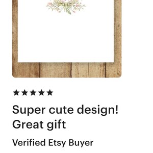 May include: A white card with a pink floral wreath and the monogram "MPD" in pink. The card is on a wood background.