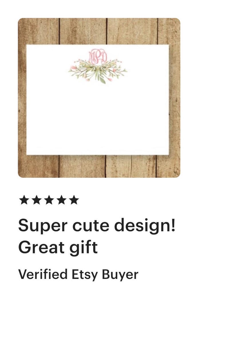 May include: A white card with a pink floral wreath and the monogram "MPD" in pink. The card is on a wood background.