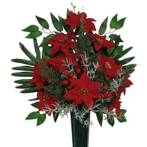 May include: A floral arrangement featuring vibrant red poinsettia blossoms, clusters of small red berries, and green foliage. The bouquet includes thin, white, frost-like sprigs and is displayed in a dark, tapered, cylindrical vase against a white background.