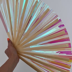 May include: A hand fan made of bamboo and iridescent plastic. The fan is open and has a rainbow-like sheen.