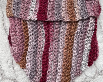 Pode incluir: Um cachecol de malha feito à mão em forma de triângulo. O cachecol apresenta listras verticais de várias cores, incluindo tons de rosa, bordô, marrom e cinza. O fio grosso cria uma aparência texturizada, perfeito para o inverno.