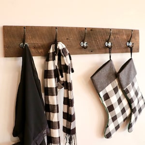 May include: A rustic wooden coat rack with four hooks, featuring a black scarf, a black and white plaid scarf, and two black and white plaid stockings with gray cuffs.