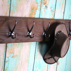 May include: A rustic wooden coat rack with six metal hooks. A brown cowboy hat hangs on one of the hooks. The rack is mounted on a light blue and white painted wall.