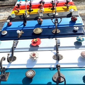 May include: A set of 10 repurposed cabinet doors painted in various colours, each with a different knob and hook. The doors are arranged vertically, creating a colourful and unique wall decor piece.