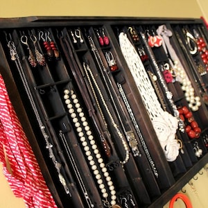 May include: A dark wooden jewelry organizer with multiple compartments and hooks. The organizer is filled with necklaces, earrings, and bracelets in various styles and colors. A red and white striped scarf hangs from the top of the organizer.