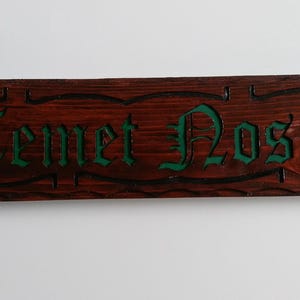May include: A wooden sign with the words "Temet Nosce" carved in green paint. The sign is dark brown and has a rustic look.