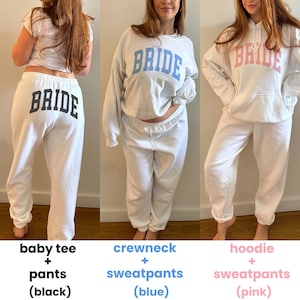 Pu&ograve; includere: Tre completi bianchi con la scritta "BRIDE" stampata. Il primo &egrave; una maglietta e pantaloni con testo nero. Il secondo &egrave; un girocollo e pantaloni della tuta con testo blu. Il terzo &egrave; una felpa con cappuccio e pantaloni della tuta con testo rosa.