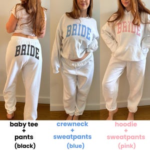 May include: Three white outfits with the word "BRIDE" printed on them. The first outfit is a baby tee and pants with black text. The second outfit is a crewneck and sweatpants with blue text. The third outfit is a hoodie and sweatpants with pink text.