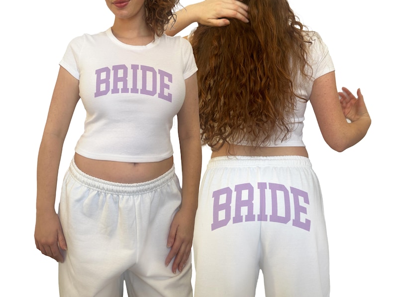 May include: White crop top and sweatpants set with the word "BRIDE" printed in lavender on the front of the top and back of the pants. The outfit is a casual style, perfect for a bridal event.