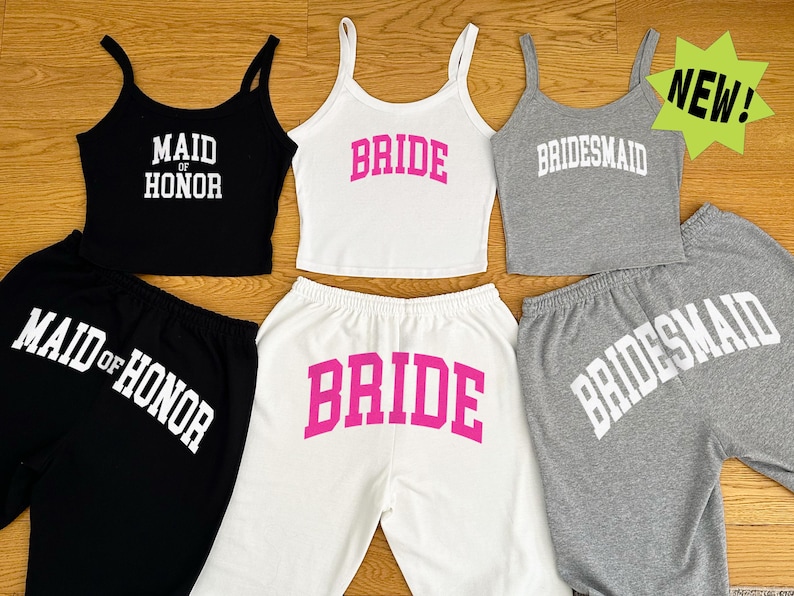 May include: A collection of matching tank tops and sweatpants sets in black, white, and gray. The tank tops and sweatpants have the words "MAID OF HONOR", "BRIDE", and "BRIDESMAID" printed on them in bold, white and pink lettering.