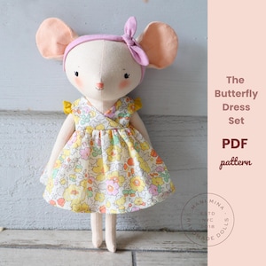 Op de afbeelding: Een stoffen muispop met een jurk met gele, roze en groene bloemen, gele mouwtjes en een lichtroze hoofdband. De tekst luidt: The Butterfly Dress Set PDF pattern. Een rond logo bevat de tekst: MANI MINA ESTD NYC 2018.