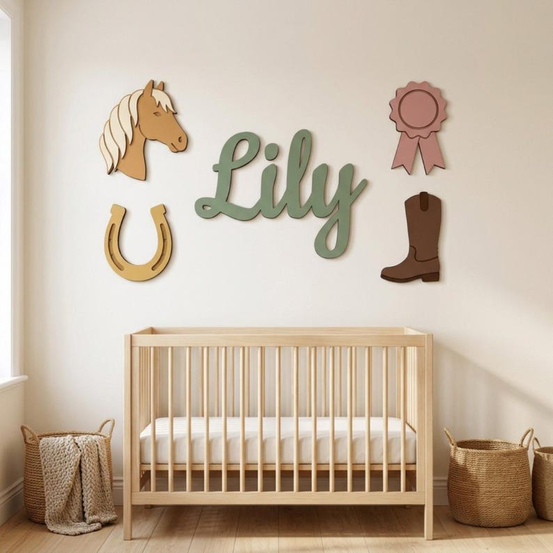 May include: A wooden crib sits below wall-mounted decor featuring the name Lily in green script, a tan horse head, a yellow horseshoe, a pink award ribbon, and a brown cowboy boot. The items are arranged on a plain wall above the light wood crib.