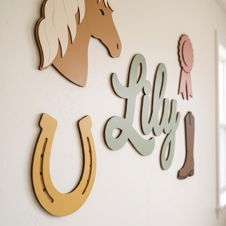 May include: A set of wall-mounted wooden cutouts featuring a tan horse head with a cream mane, a mustard yellow horseshoe, the name Lily in sage green script, a dusty pink award ribbon, and a brown cowboy boot silhouette.