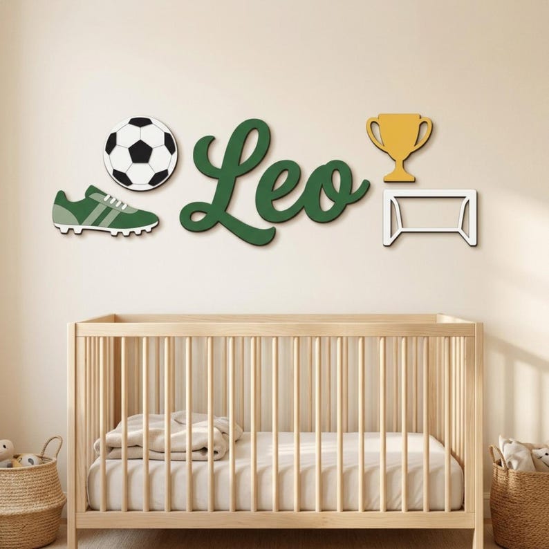 May include: A wall decor set featuring a black and white soccer ball, a green soccer cleat, the name Leo in dark green cursive script, a gold trophy, and a white soccer goal outline, all arranged horizontally above a wooden crib.