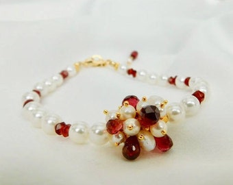 May include: A delicate bracelet made with white pearls and red gemstones. The bracelet features a cluster of red gemstones and pearls in the center.
