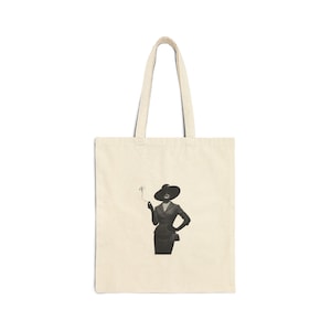 May include: Cream-colored tote bag featuring a black and white illustration of a person in a suit and hat, holding a cigarette. The bag has a simple design with a rectangular shape and two handles.