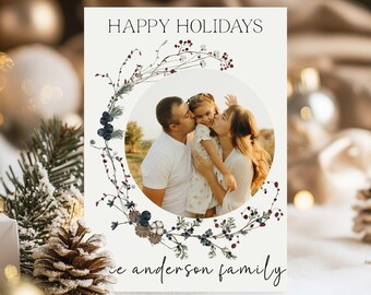 May include: A holiday card with the text "HAPPY HOLIDAYS" and a family photo inside a floral wreath. The card features a family of three, with the family name written at the bottom. The wreath includes berries and leaves.