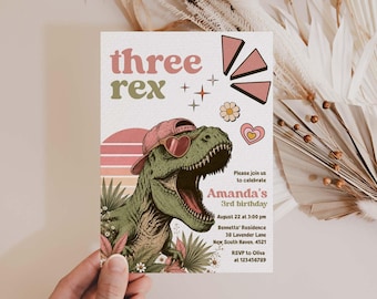 May include: A rectangular birthday invitation card featuring a green T-Rex wearing a pink baseball cap and heart-shaped sunglasses. The text reads three rex, Amanda's 3rd birthday, August 22 at 3:00 pm, Bennett's Residence, 38 Lavender Lane, New South Haven, 4521.
